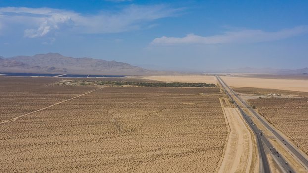 Aerial view of a desert landscape with a long highway stretching towards distant mountains under a clear blue sky in the United States.