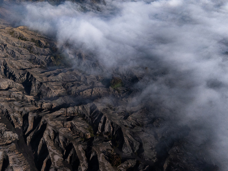 Aerial view of Lautan Pasir Bromo volcanic landscape covered by thick rolling clouds and rugged terrain in Kecamatan Sukapura Jawa Timur Indonesia.