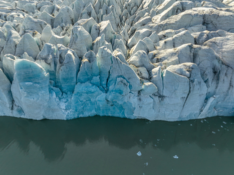 Aerial view of the rugged surface of a glacier with deep blue crevasses and ice formations meeting the dark glacial water in Iceland. Aerial view of the rugged surface of a glacier with deep blue crevasses and ice formations meeting the dark glacial water in Iceland.