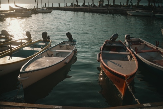 View of Lake Garda with small motorboats moored in the harbor and sunlight reflecting on the calm water during golden hour Italy. View of Lake Garda with small motorboats moored in the harbor and sunlight reflecting on the calm water during golden hour Italy.