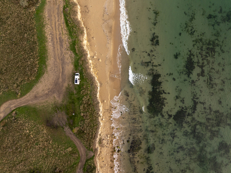 Aerial view of a white camper van parked on a dirt path next to a sandy beach and the clear waters of the Black Sea in Nessebar Burgas Bulgaria. Aerial view of a white camper van parked on a dirt path next to a sandy beach and the clear waters of the Black Sea in Nessebar Burgas Bulgaria.