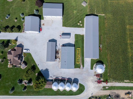 Aerial view of a farmstead featuring multiple metal roofed barns grain silos and a gravel driveway surrounded by green lawns and cornfields in Lakeshore Ontario Canada. Aerial view of a farmstead featuring multiple metal roofed barns grain silos and a gravel driveway surrounded by green lawns and cornfields in Lakeshore Ontario Canada.