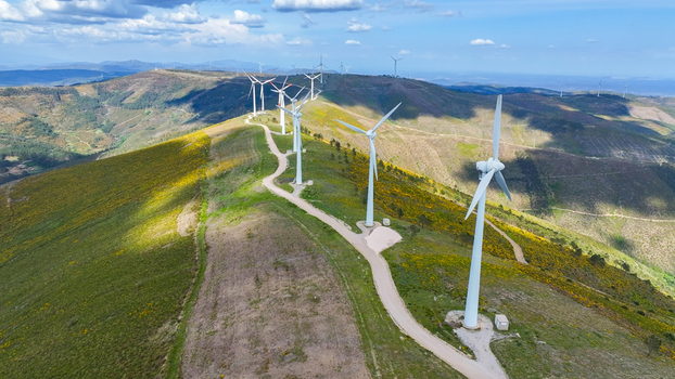 Aerial view of wind turbines situated along a ridge on rolling green hills with a dirt access road under a blue sky in Lisbon Lisbon Portugal. Aerial view of wind turbines situated along a ridge on rolling green hills with a dirt access road under a blue sky in Lisbon Lisbon Portugal.
