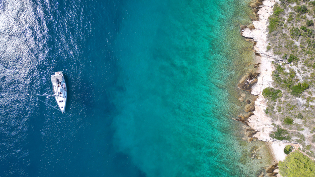 Aerial view of a white sailboat anchored in the turquoise waters of a bay along a rocky coastline with green vegetation in Necujam Split Dalmatia County Croatia. Aerial view of a white sailboat anchored in the turquoise waters of a bay along a rocky coastline with green vegetation in Necujam Split Dalmatia County Croatia.