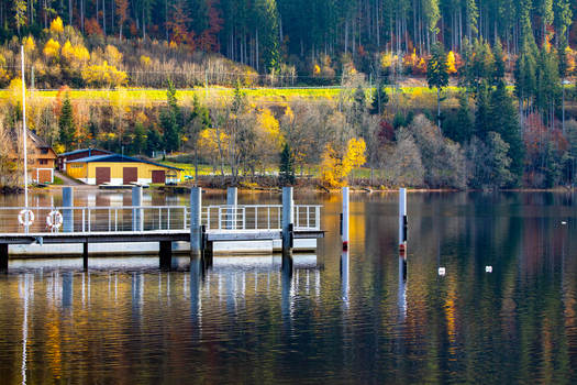 View of a wooden pier on a calm lake with autumn forest and buildings on the shore in Breitnau Baden Wurttemberg Germany. View of a wooden pier on a calm lake with autumn forest and buildings on the shore in Breitnau Baden Wurttemberg Germany.