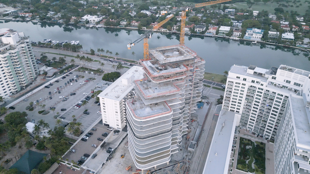 Aerial view of a high rise building under construction with tall cranes surrounded by residential buildings a canal and parking areas in Miami Beach Florida United States. Aerial view of a high rise building under construction with tall cranes surrounded by residential buildings a canal and parking areas in Miami Beach Florida United States.