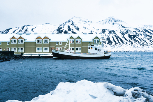 View of a fishing boat docked at the harbor in front of Hotel Siglo with snow covered mountains in the background in Siglufjordur Fjallabyggd Iceland.