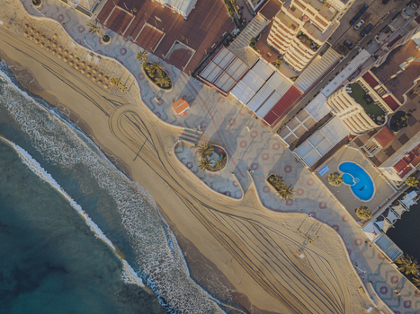 Aerial view of the sandy beach and patterned promenade with modern apartment buildings a swimming pool and tire tracks on the sand in Calp Valencian Community Spain. Aerial view of the sandy beach and patterned promenade with modern apartment buildings a swimming pool and tire tracks on the sand in Calp Valencian Community Spain.