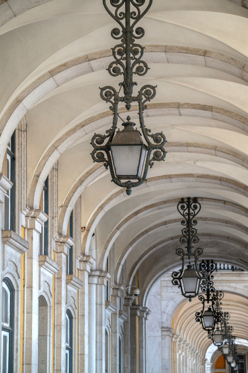 View of ornate wrought iron lanterns hanging from the vaulted stone arcade of Praca do Comercio in Lisbon Lisbon Portugal.