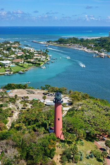Aerial view of the red Jupiter Inlet Lighthouse surrounded by lush tropical vegetation overlooking the blue waters of the inlet with boats Jupiter Florida United States. Aerial view of the red Jupiter Inlet Lighthouse surrounded by lush tropical vegetation overlooking the blue waters of the inlet with boats Jupiter Florida United States.