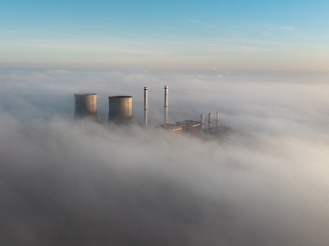 Aerial view of the RWE Clauscentrale power plant with cooling towers and chimneys emerging from a thick layer of morning fog under a clear blue sky in Maasbracht Limburg Netherlands. Aerial view of the RWE Clauscentrale power plant with cooling towers and chimneys emerging from a thick layer of morning fog under a clear blue sky in Maasbracht Limburg Netherlands.