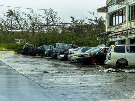 San Jose Tinian Northern Mariana Islands 06 July 2026 View of damaged vehicles and storm debris in a parking lot after a super typhoon with broken trees and a weathered building. San Jose Tinian Northern Mariana Islands 06 July 2026 View of damaged vehicles and storm debris in a parking lot after a super typhoon with broken trees and a weathered building.