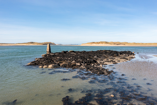 Aerial view of Ballyness Bay featuring a rocky outcrop with a stone beacon surrounded by tidal waters and sandy dunes in Ballyness County Donegal Ireland. Aerial view of Ballyness Bay featuring a rocky outcrop with a stone beacon surrounded by tidal waters and sandy dunes in Ballyness County Donegal Ireland.