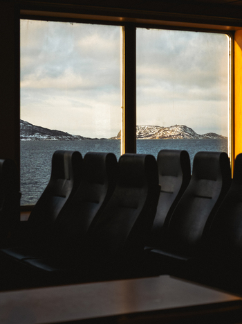 View of dark plush seats lined up near a window overlooking the serene snow touched islands in the distance Brensholmen Troms Norway. View of dark plush seats lined up near a window overlooking the serene snow touched islands in the distance Brensholmen Troms Norway.