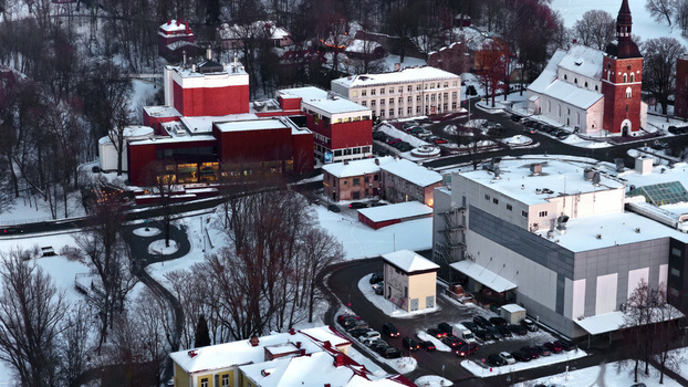 Aerial view of a snow covered town featuring a prominent red theater building a historic church with a spire and surrounding urban infrastructure Latvija. Aerial view of a snow covered town featuring a prominent red theater building a historic church with a spire and surrounding urban infrastructure Latvija.