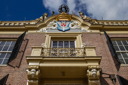 View of Castle Groeneveld facade featuring an ornate balcony and heraldic coat of arms against a blue sky in Baarn Utrecht Netherlands.