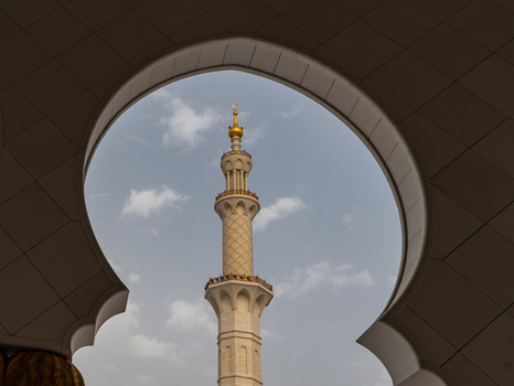 View of a tall ornate minaret with a golden crescent moon on top framed by a white scalloped archway under a blue sky in Dubai Dubai United Arab Emirates. View of a tall ornate minaret with a golden crescent moon on top framed by a white scalloped archway under a blue sky in Dubai Dubai United Arab Emirates.