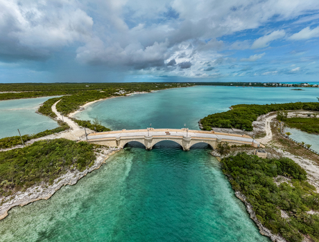 Aerial view of the stone bridge at Crab Cay spanning turquoise waters between lush green islands under a cloudy sky in Exuma Exuma The Bahamas. Aerial view of the stone bridge at Crab Cay spanning turquoise waters between lush green islands under a cloudy sky in Exuma Exuma The Bahamas.