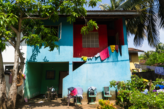 View of a colorful two story house with bright blue and red walls laundry hanging on the balcony and a wheelchair in the shaded ground floor Galle Southern Province Sri Lanka.