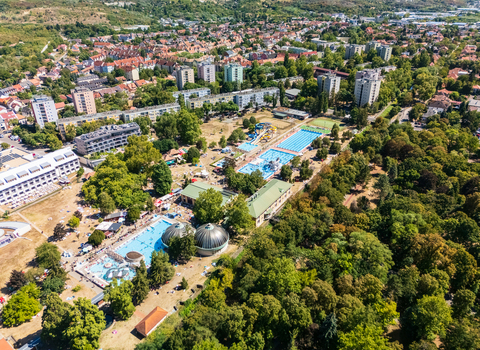 Aerial view of Eger s outdoor thermal bath complex with swimming pools and waterslides surrounded by parkland apartment buildings and city streets in Hungary. Aerial view of Eger s outdoor thermal bath complex with swimming pools and waterslides surrounded by parkland apartment buildings and city streets in Hungary.