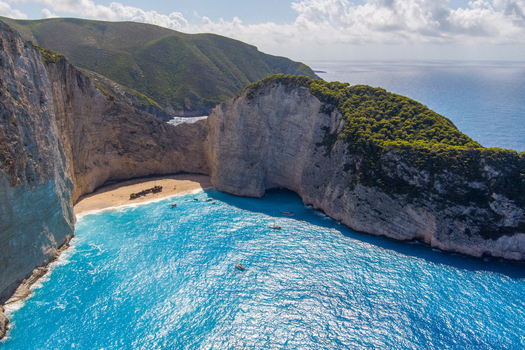 Aerial view of Navagio Beach featuring the iconic shipwreck on the sandy shore surrounded by towering limestone cliffs and vibrant turquoise waters in Zakynthos Navagio Greece.