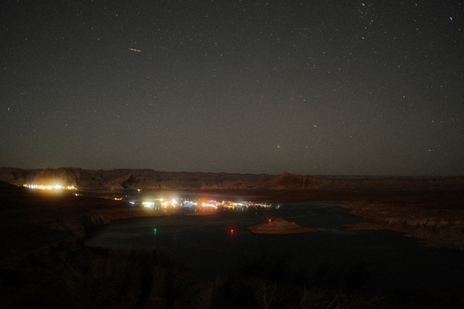 View of the illuminated shoreline of Lake Powell at night under a clear starry sky with distant desert rock formations Lake Powell Arizona United States.