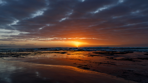 Aerial view of the sun setting over the rocky coastline of Hartenbos beach with dramatic clouds and golden reflections on the water Mossel Bay Western Cape South Africa. Aerial view of the sun setting over the rocky coastline of Hartenbos beach with dramatic clouds and golden reflections on the water Mossel Bay Western Cape South Africa.