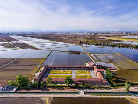 Aerial view of Tenuta Colombara historic farm estate surrounded by flooded rice fields under a clear blue sky in Livorno Ferraris Piemonte Italy.
