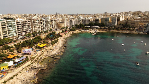 Aerial view of the coastline of Sliema with modern apartment buildings a rocky beach turquoise water and small boats in Malta. Aerial view of the coastline of Sliema with modern apartment buildings a rocky beach turquoise water and small boats in Malta.