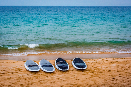 View of four stand up paddleboards resting on the sandy beach with gentle waves rolling onto the shore in Maui County Hawaii United States.