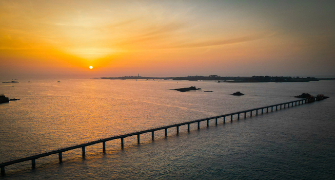Aerial view of a long pier stretching into the sea reflecting the vibrant hues of the setting sun near &Icirc;le de Batz Roscoff Brittany France.
