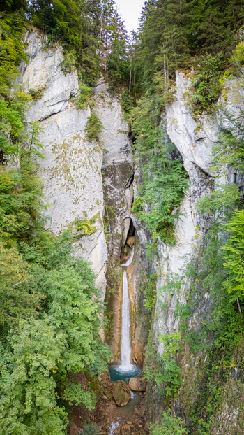 Aerial view of Grandvillard Waterfall cascading down a narrow rocky gorge surrounded by lush green forest and steep limestone cliffs Grandvillard Fribourg Switzerland.