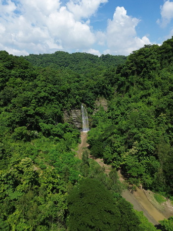 Aerial view of the waterfall cascading through the dense lush green forest with a small stream flowing below in Sitakund Chittagong Division Bangladesh. Aerial view of the waterfall cascading through the dense lush green forest with a small stream flowing below in Sitakund Chittagong Division Bangladesh.