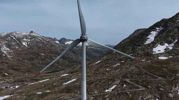 Aerial view of San Gottardo wind Park with a large wind turbine spinning over rocky mountain slopes and winding roads in Airolo Ticino Switzerland.