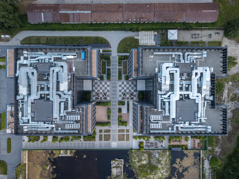 Aerial view of a modern office complex with symmetrical buildings featuring extensive rooftop HVAC ductwork a central paved courtyard with a checkerboard pattern and a small pond in Poland. Aerial view of a modern office complex with symmetrical buildings featuring extensive rooftop HVAC ductwork a central paved courtyard with a checkerboard pattern and a small pond in Poland.