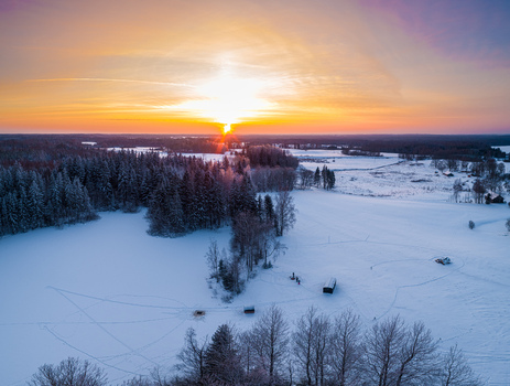 Aerial view of a snow covered landscape with dense pine forests and open fields under a vibrant sunset sky in Latvia. Aerial view of a snow covered landscape with dense pine forests and open fields under a vibrant sunset sky in Latvia.