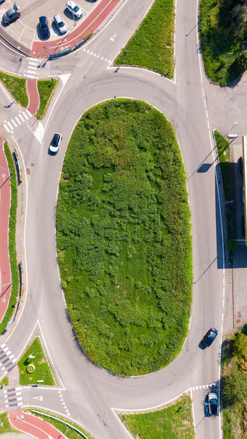 Aerial view of a traffic roundabout with a central green island surrounded by asphalt roads and moving cars in Milan Lombardy Italy.