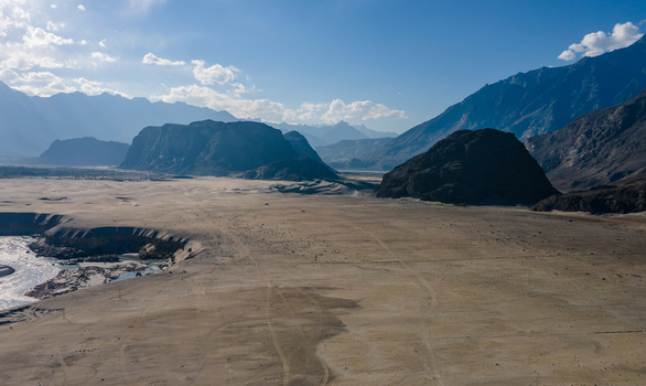 Aerial view of Sarfaranga Cold Desert Shigar featuring vast sandy dunes rugged mountains and a winding river under a clear blue sky in Skardu Gilgit Pakistan.