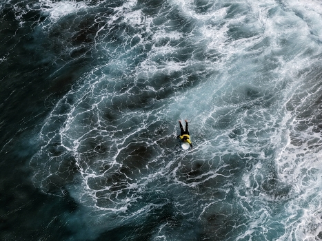 Aerial view of a surfer paddling through white ocean foam and dark blue waves at Praia do Areal de Santa Barbara in Ribeira Grande Acores Portugal. Aerial view of a surfer paddling through white ocean foam and dark blue waves at Praia do Areal de Santa Barbara in Ribeira Grande Acores Portugal.
