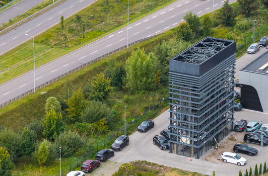 Aerial view of a modern automated car parking tower structure with multiple levels of parked vehicles surrounded by green trees and a nearby highway in Gdansk Pomeranian Voivodeship Poland. Aerial view of a modern automated car parking tower structure with multiple levels of parked vehicles surrounded by green trees and a nearby highway in Gdansk Pomeranian Voivodeship Poland.