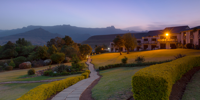 View of a stone pathway winding through a manicured lawn towards a lodge building at dusk with mountains in the background in South Africa.