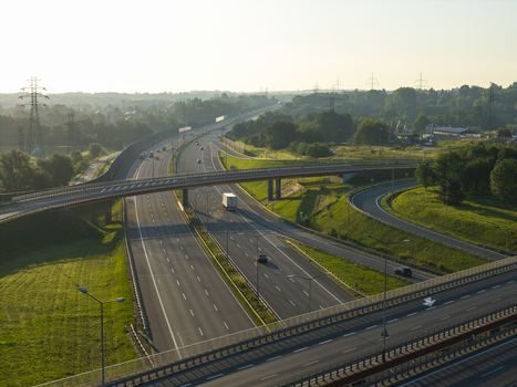 Aerial view of a highway interchange with vehicles driving on asphalt roads surrounded by green fields trees and power lines in Krakow Lesser Poland Voivode Poland.