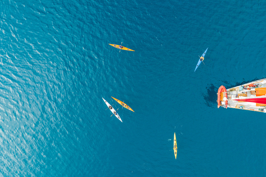 Aerial view of several colorful kayaks paddling near a sailboat in the deep blue waters of Uummannaq Kitaa Greenland. Aerial view of several colorful kayaks paddling near a sailboat in the deep blue waters of Uummannaq Kitaa Greenland.