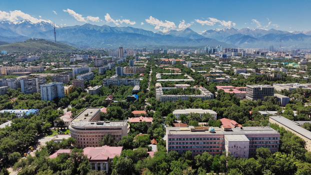 Aerial view of Almaty featuring dense urban architecture lush green trees and the Trans Ili Alatau mountains in the background under a clear blue sky in Almaty Almaty Region Kazakhstan.