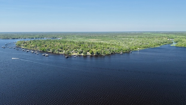 Aerial view of Sixmile Creek with wooden docks along the lush forested shoreline under a clear blue sky in St. Johns County Florida United States.