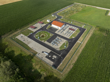 Aerial view of a natural gas facility with pipelines a small building with an orange roof and paved access roads surrounded by lush green corn fields in Finsing Bavaria Germany.