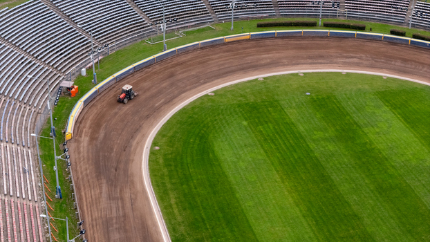 Aerial view of a tractor grooming the dirt track at the speedway stadium with empty seating and a green infield in Gdansk Poland.