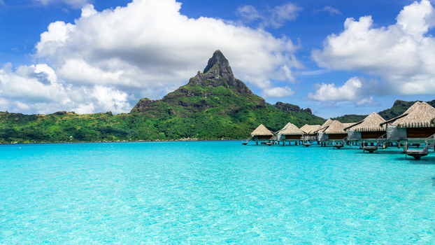 View of the iconic Mount Otemanu rising above turquoise lagoon waters and traditional overwater bungalows in Bora Bora Leeward Islands French Polynesia.