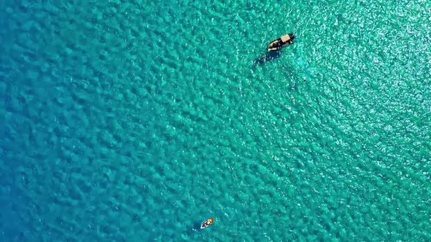 Aerial view of boat and paddleboard in turquoise sea Greece.