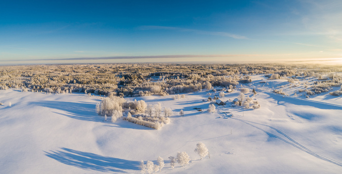 Aerial view of a vast snow covered landscape with frost covered trees and a small rural homestead under a clear blue sky in Latvia. Aerial view of a vast snow covered landscape with frost covered trees and a small rural homestead under a clear blue sky in Latvia.